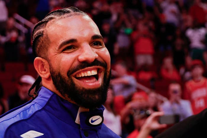 Drake smiles, wearing a sports jacket, surrounded by fans