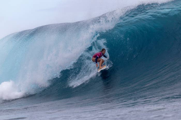 A surfer rides a massive wave on a surfboard. The wave curls overhead, creating a dramatic scene of action and skill