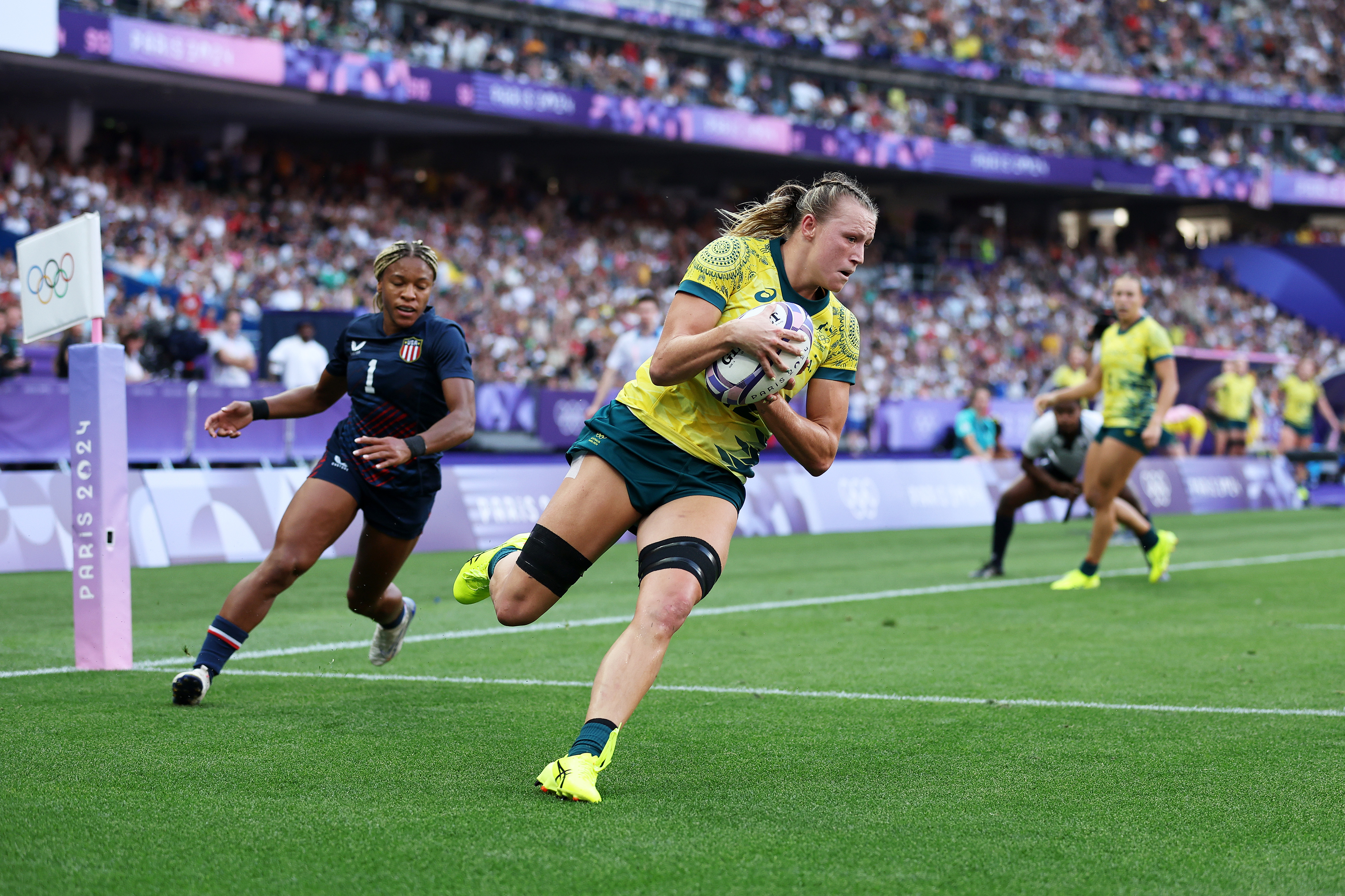 Australian rugby player running with the ball during a match at a stadium. An opponent from the other team attempts to catch up