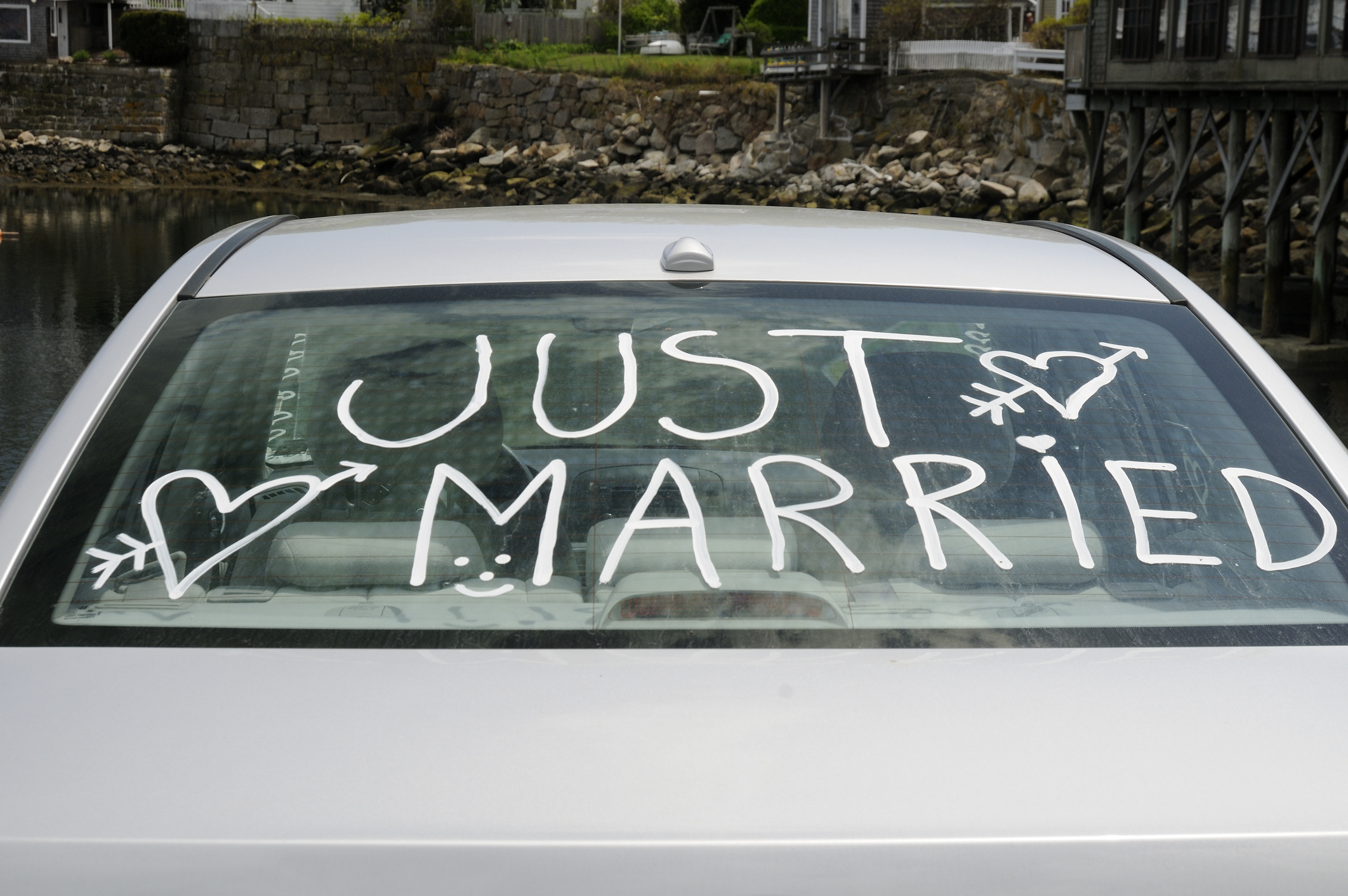 The back window of a car with &quot;Just Married&quot; written on it in white paint, adorned with hearts and arrows