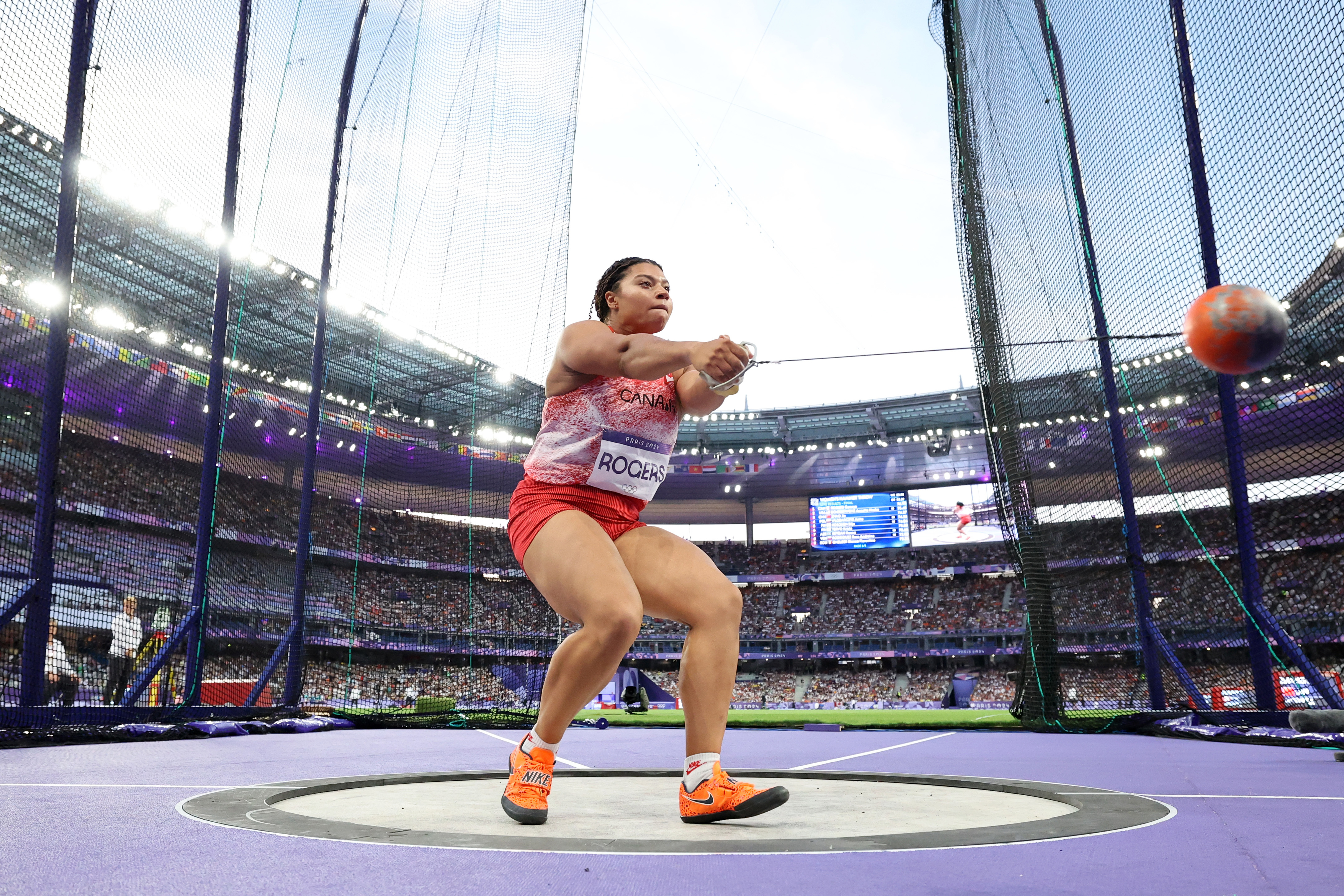 Camryn Rogers, wearing athletic gear, prepares to throw a hammer during a track and field event in a stadium filled with spectators