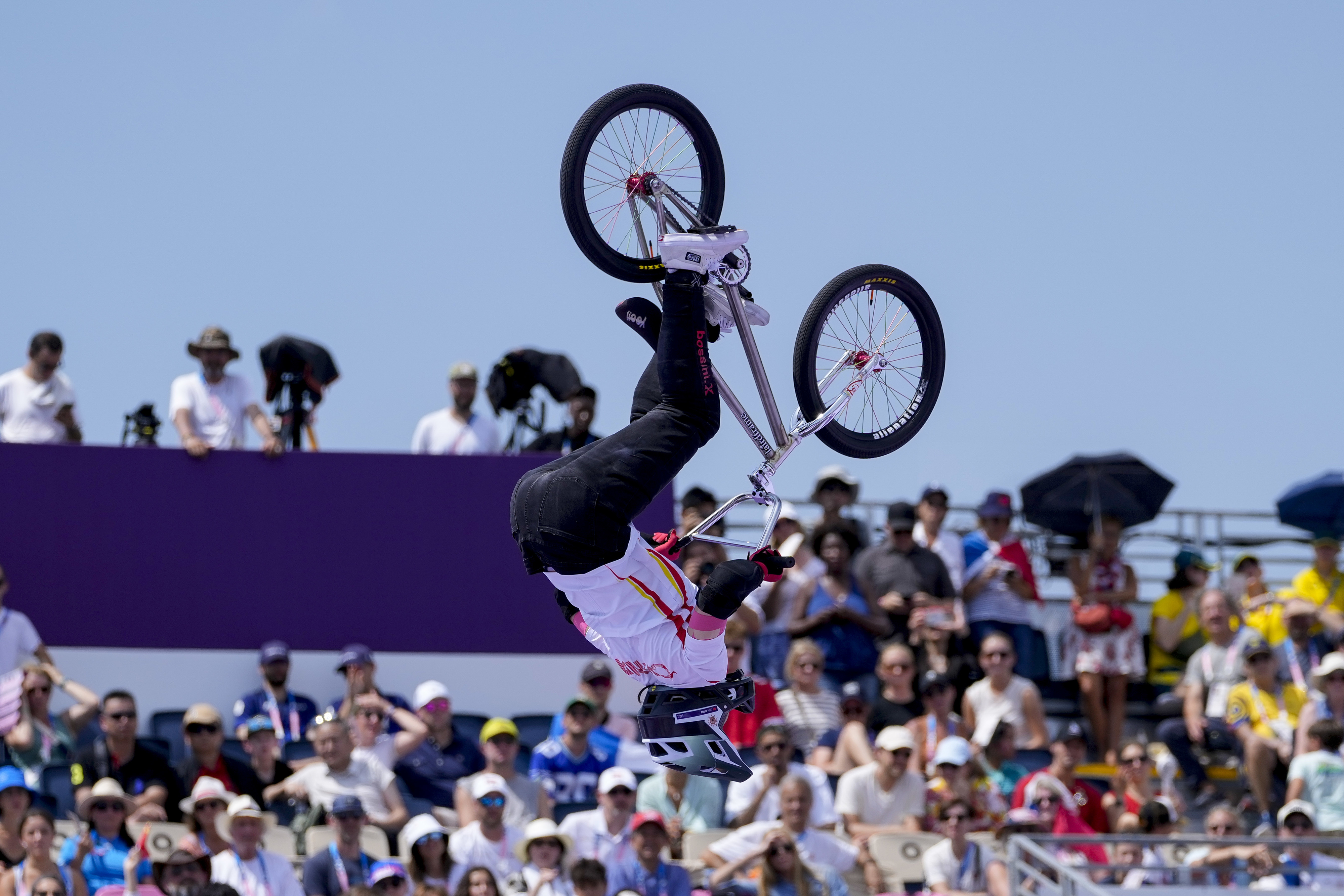 A cyclist performing an aerial stunt on a BMX bike in front of a large, attentive crowd during a competitive event