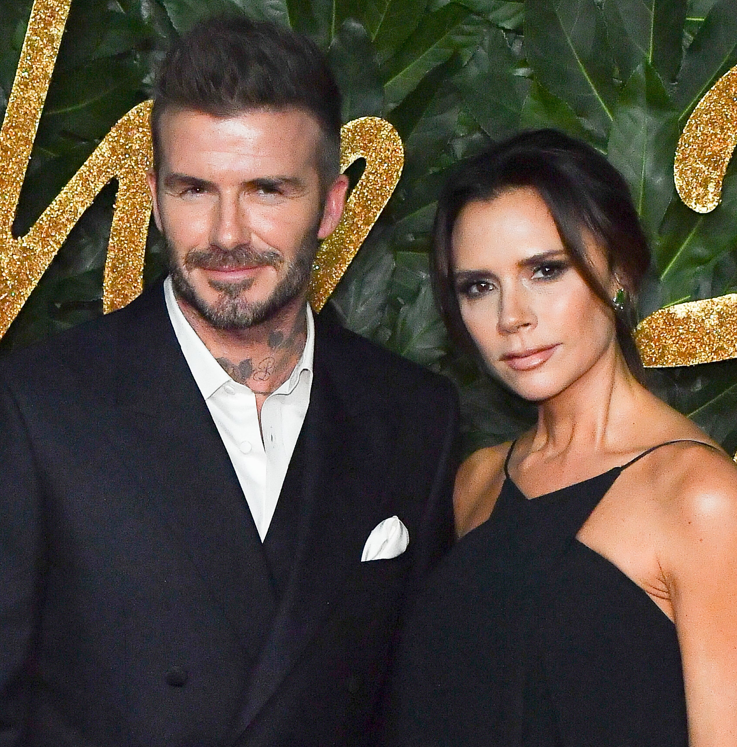 David Beckham and Victoria Beckham pose together at an event. David wears a black suit, while Victoria is in a stylish black dress