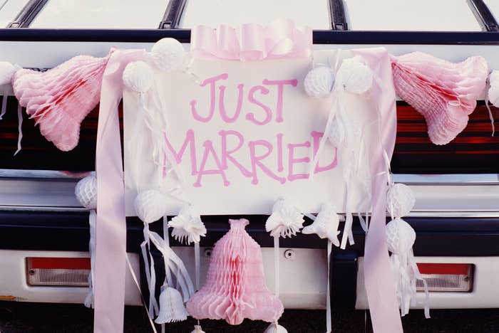 Back of a car decorated with a "Just Married" sign and various paper decorations, including bells and streamers
