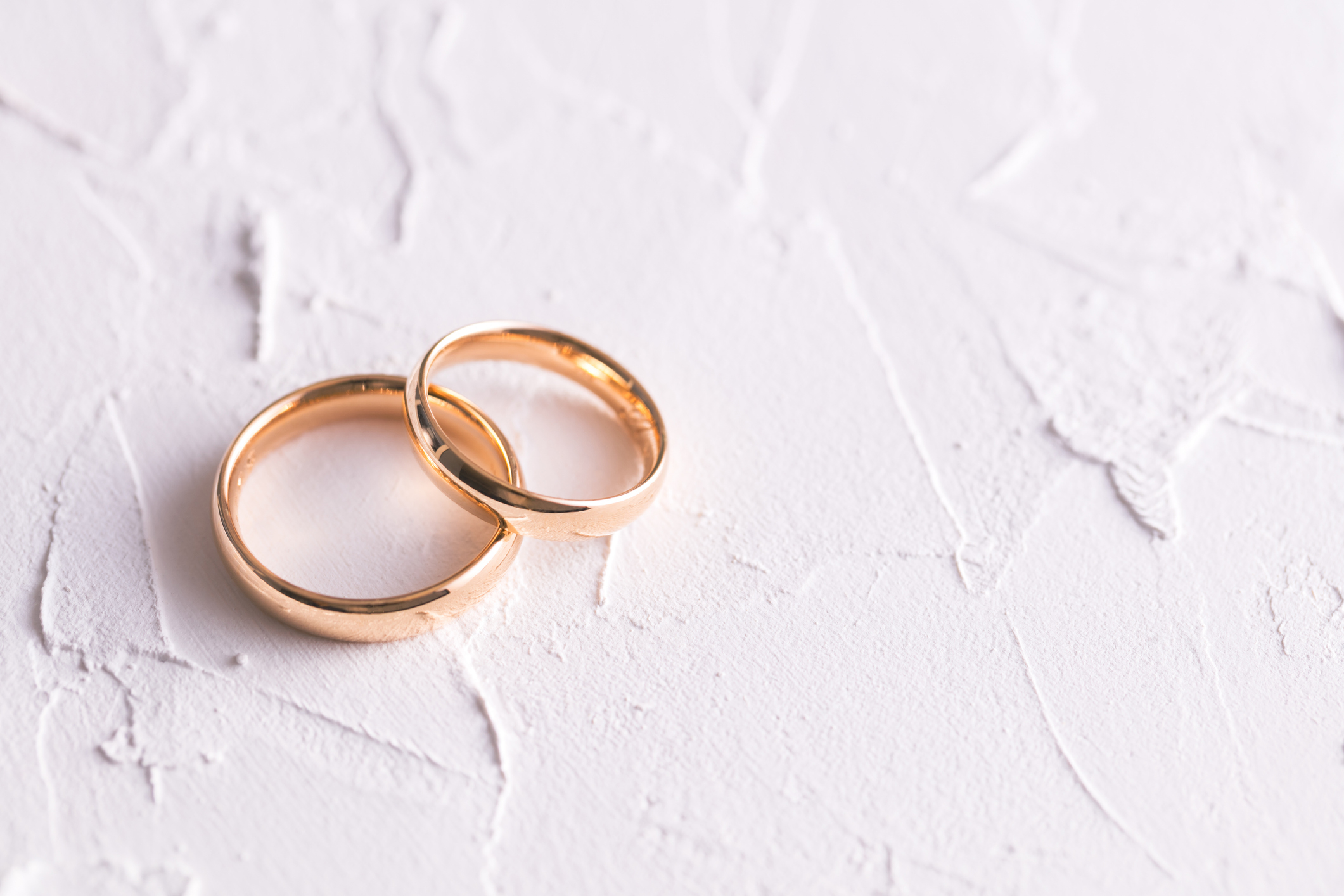 Two gold wedding rings rest atop a textured white surface, overlapping slightly