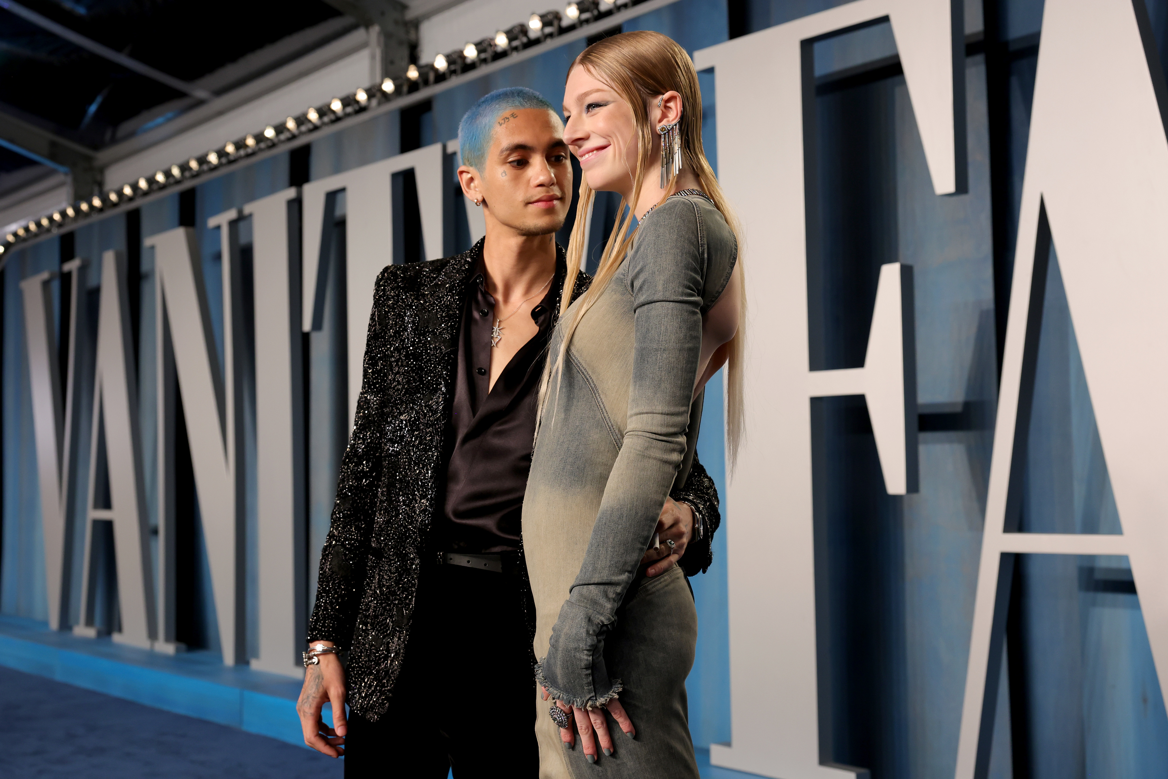 Dominic Fike in a glittery black suit and Hunter Schafer in a long-sleeve, form-fitting dress pose together at a Vanity Fair event