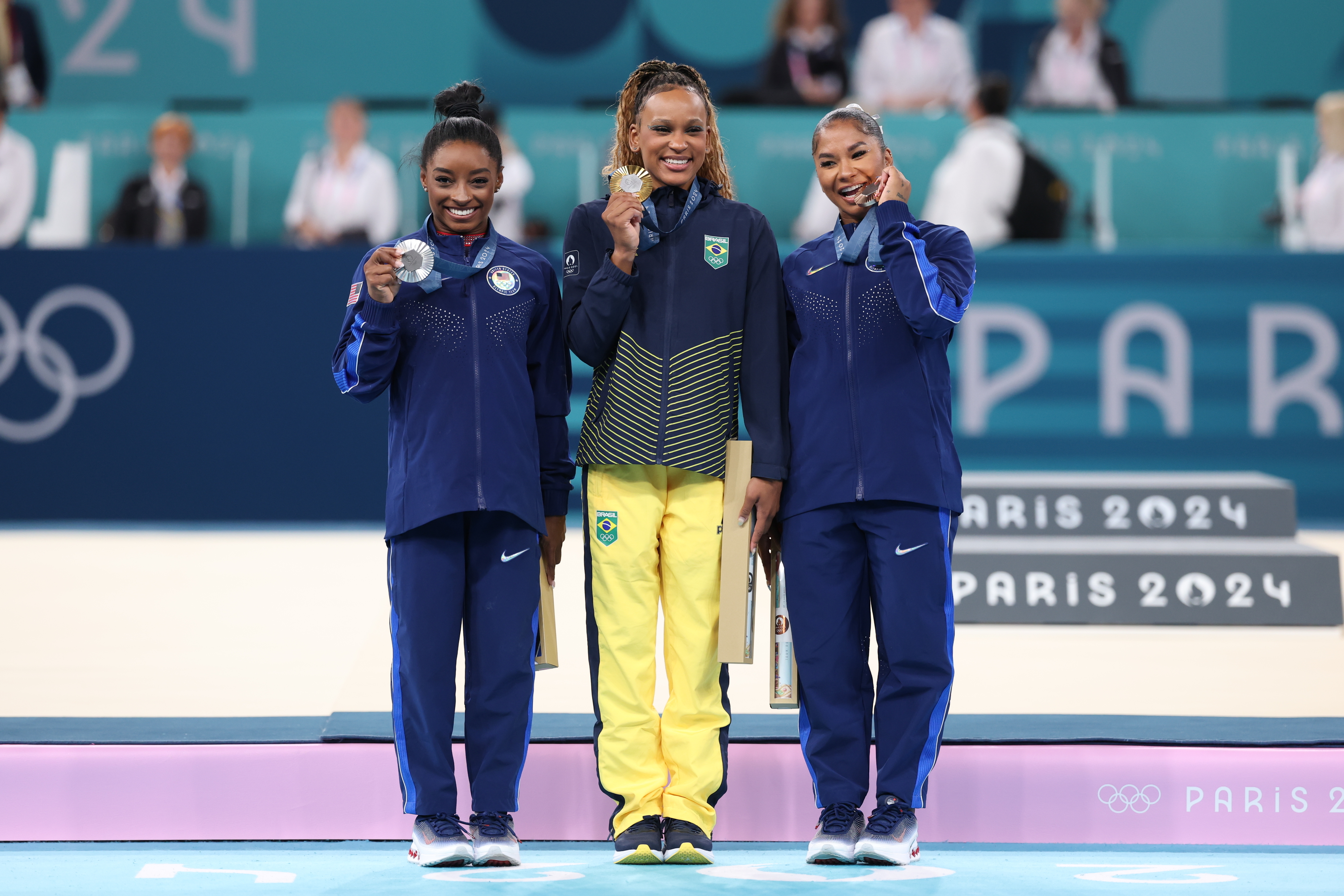 Simone Biles, Rebeca Andrade, and Shilese Jones pose with their medals on the winners' podium at the Paris 2024 gymnastics event