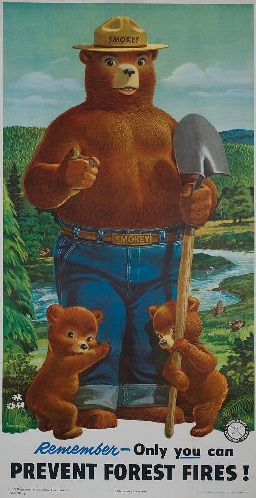 Smokey Bear stands with two bear cubs near a forest river holding a shovel. Text: "Remember - Only you can prevent forest fires!"