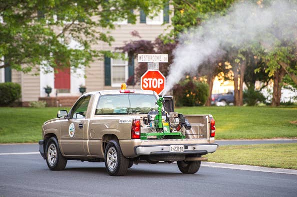 A truck sprays insecticide in a residential neighborhood, aiming to control the mosquito population