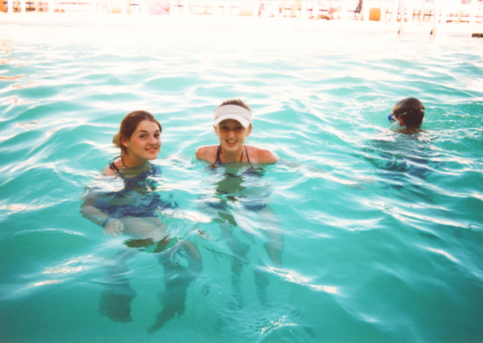Two girls swimming in a pool and smiling at the camera