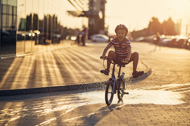 A boy rides a bicycle while doing a trick. The sun is setting, casting long shadows on the street