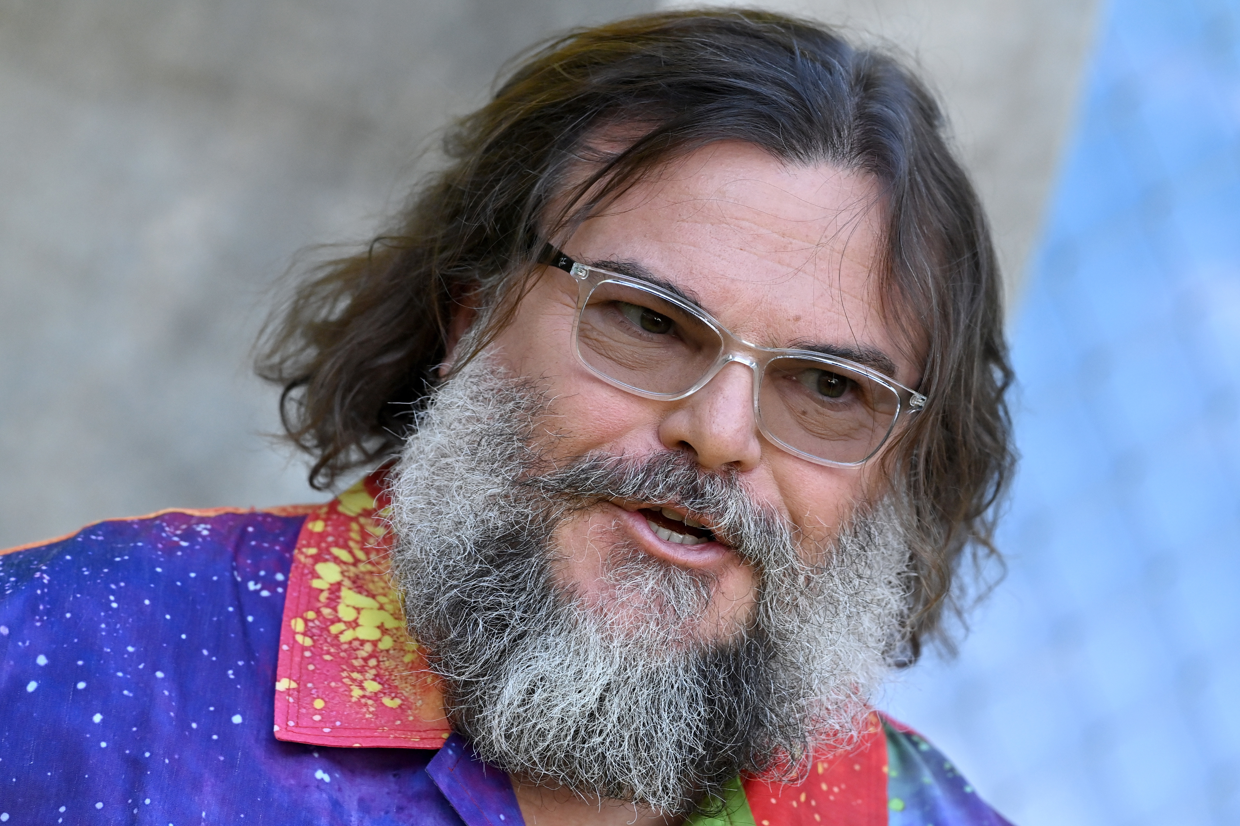 Jack Black, with a bushy beard and clear glasses, is wearing a colorful, patterned shirt in a close-up photo