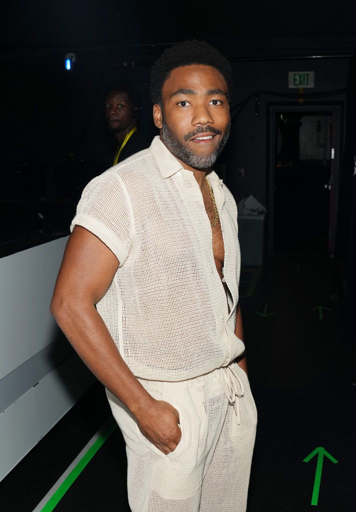 Donald Glover stands in a stylish see-through outfit backstage at an event