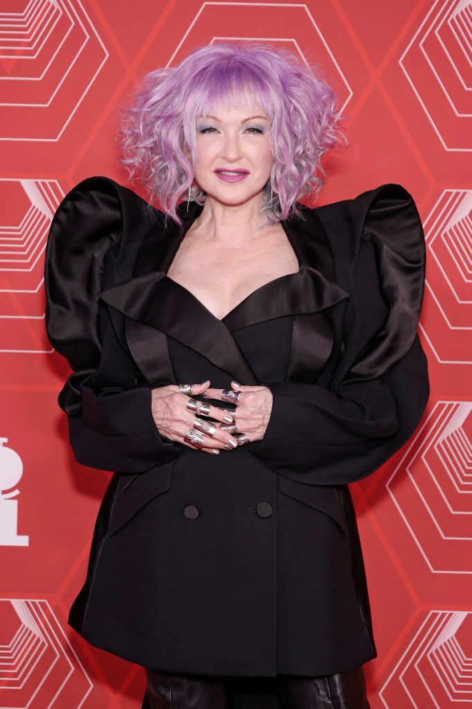 Cyndi Lauper on the red carpet wearing a black structured jacket with voluminous sleeves and silver rings