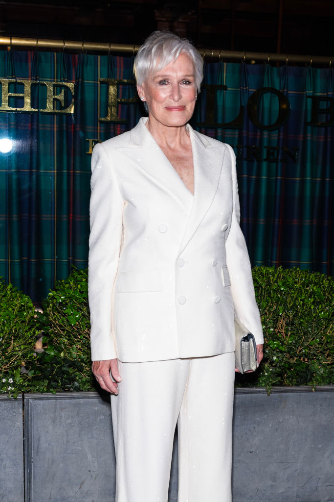 Glenn Close on the red carpet, wearing an elegant white pantsuit, holding a clutch