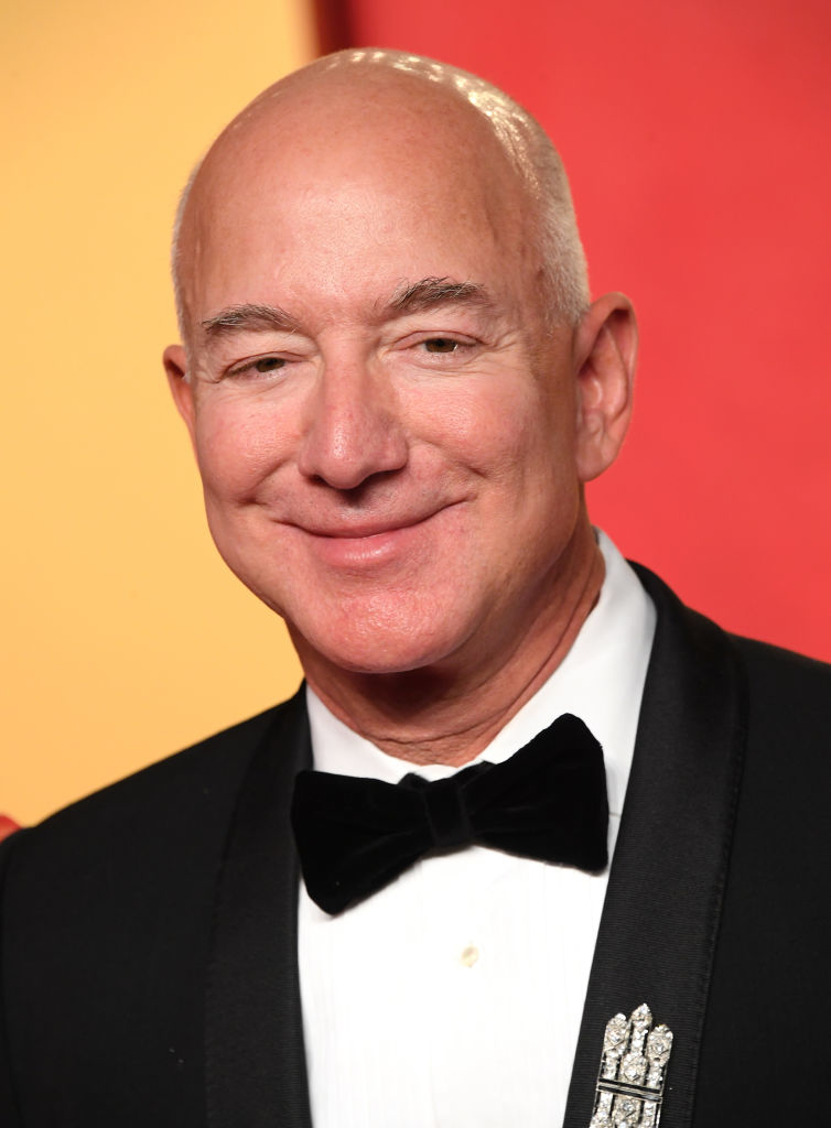 Jeff Bezos is wearing a formal black tuxedo with a bow tie, smiling at the camera against a plain background