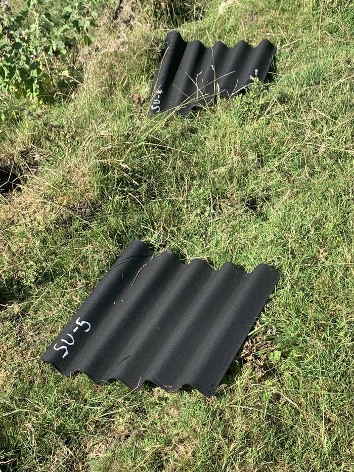 Two black corrugated sheets labeled "SU-5" lie on grassy ground outdoors