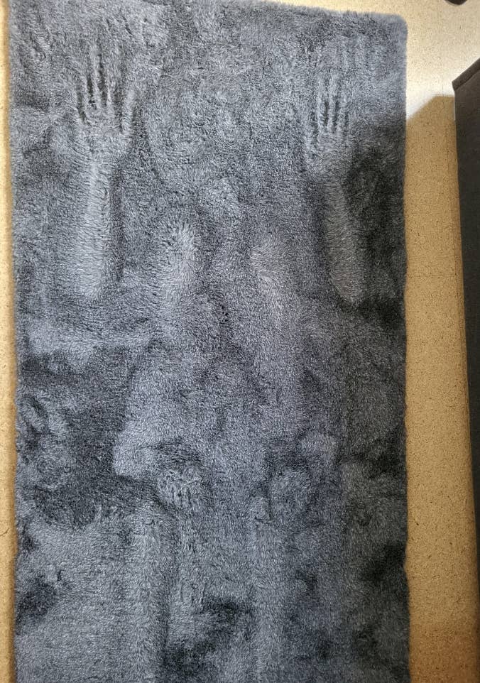 Imprint of two hands and a person's torso, including a face and upper body, pressed into a thick, textured fabric. No text is visible