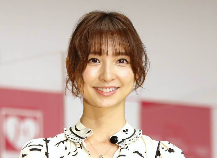 白いフリルのドレスを着た女性が、花束とトロフィーを持って笑顔で立っています。