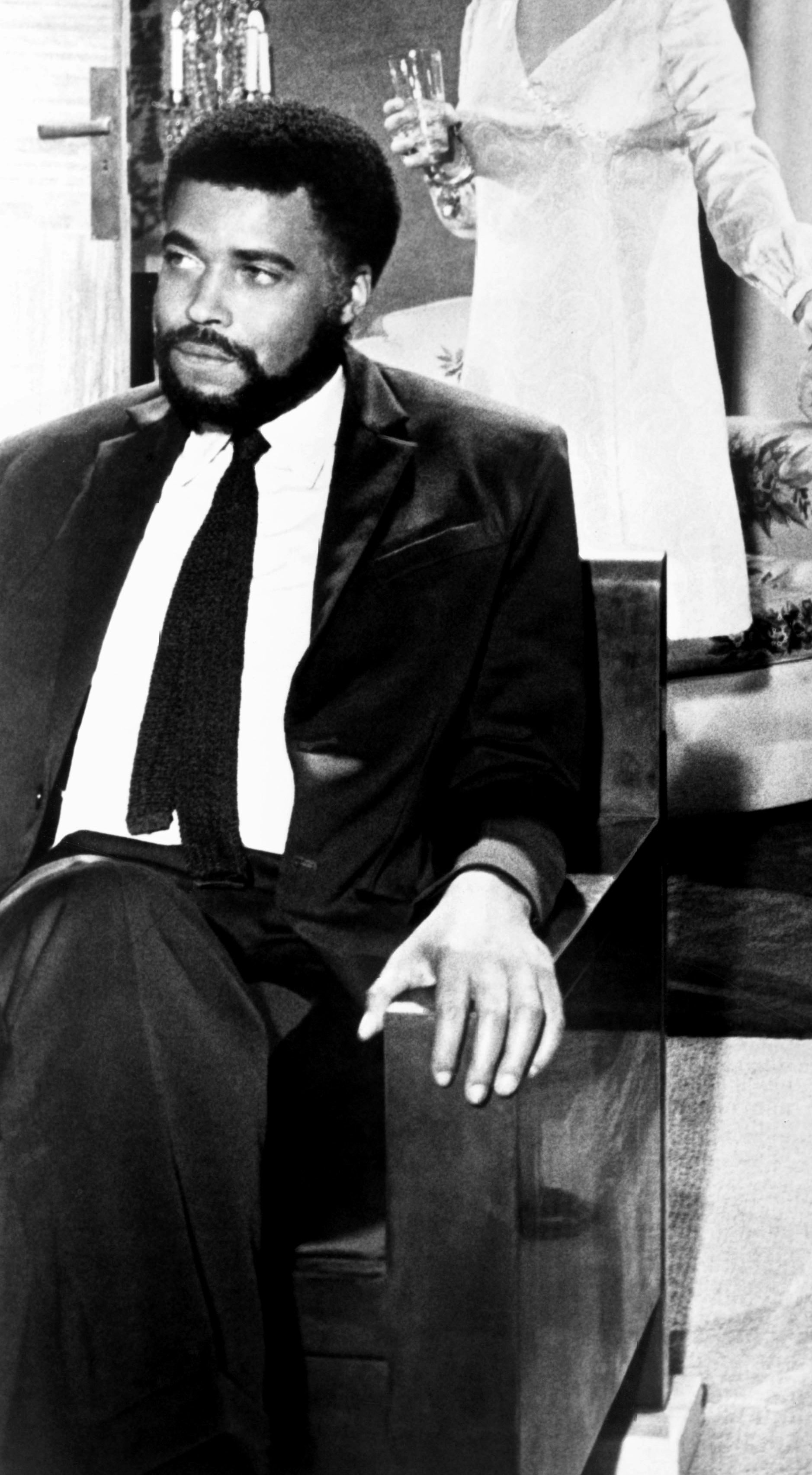A young James Earl Jones in a suit tie sitting in a scene from 1967 film "The Comedians"