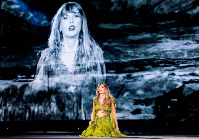 Taylor Swift performing on stage in a flowing dress with a large black-and-white backdrop showing her image