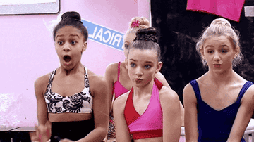 Nia Sioux, Kendall Vertes, and Chloe Lukasiak expressing surprise. They are wearing dance outfits and are inside a dance studio