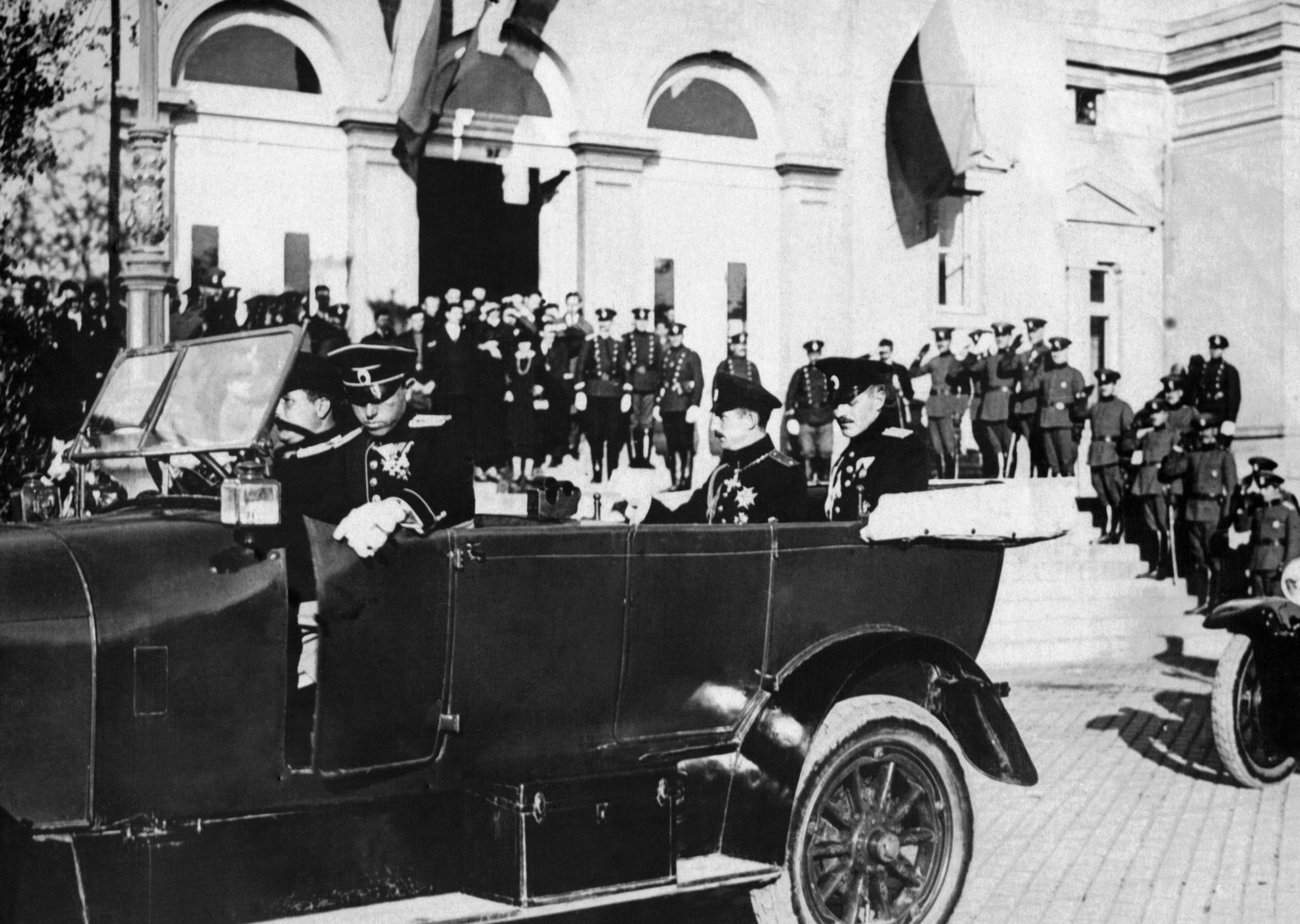 Historical photograph depicting uniformed officials arriving in an open-top vehicle, greeted by a large assembly of soldiers in front of a building in 1920 in Bulgaria