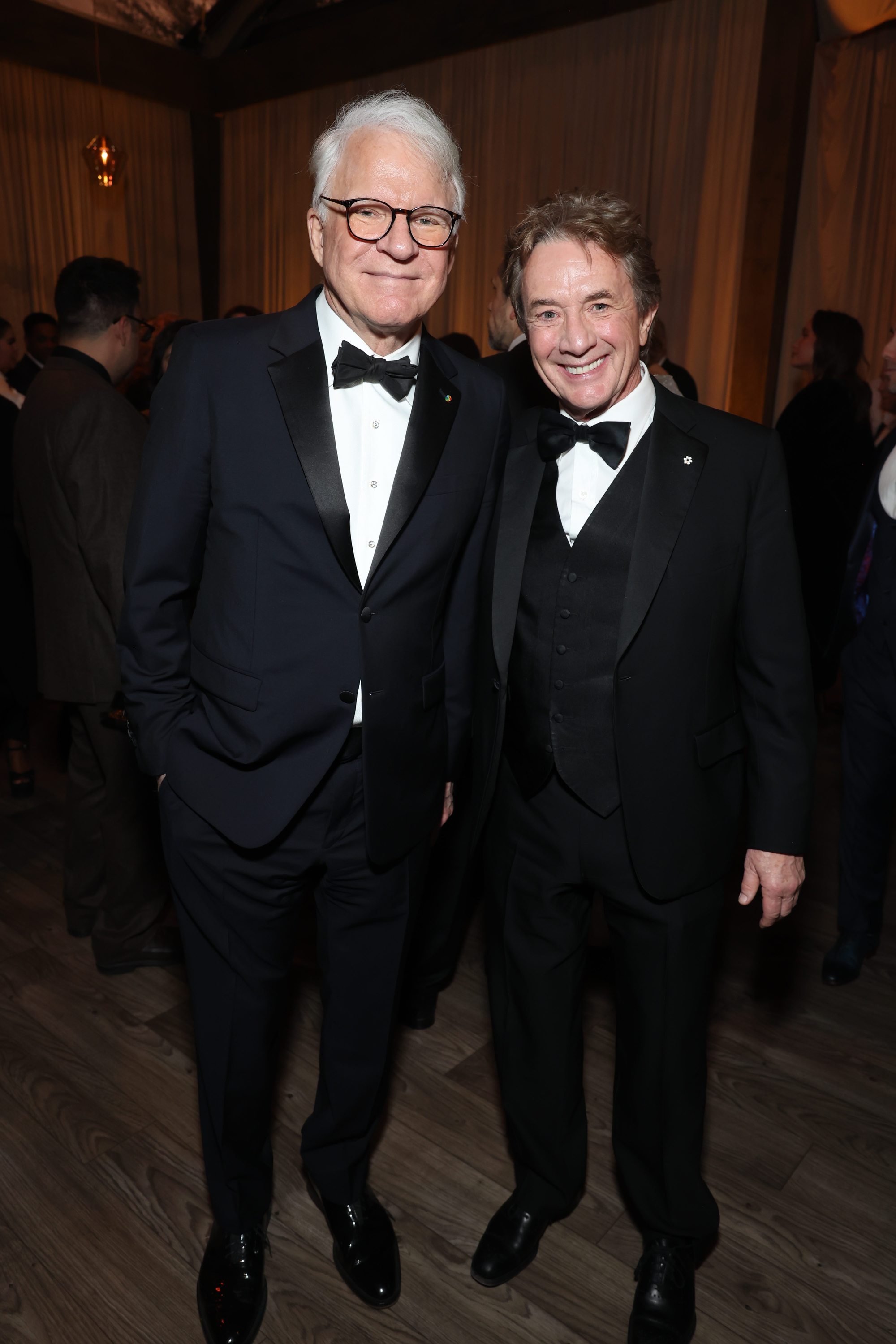 Steve Martin and Martin Short are dressed in formal black suits with bow ties, standing together at an event