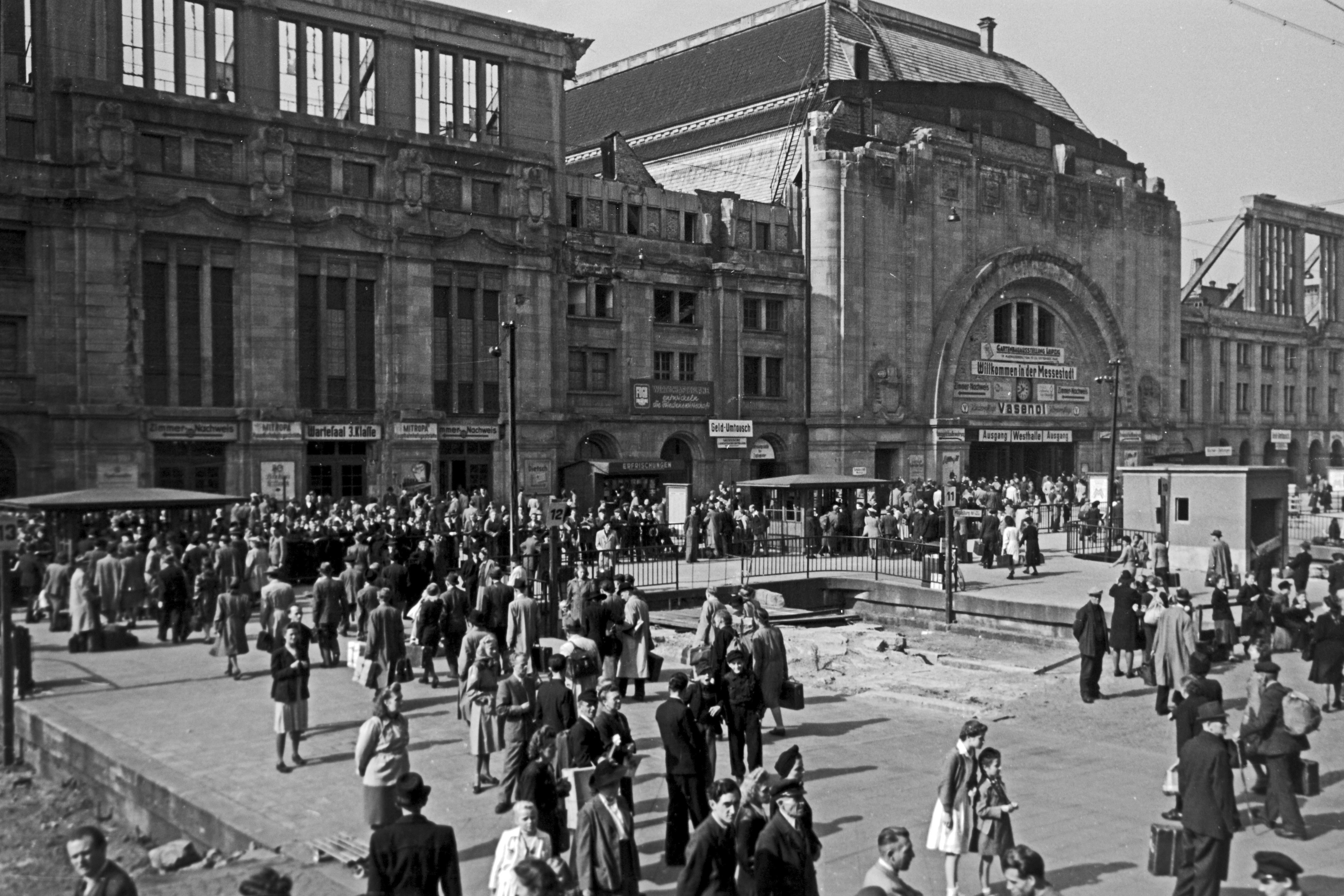 A bustling crowd at the Leipziger railway station, Saxony, Germany, 1948. Ppeople walk in and around a large train station with an ornate façade and arched windows