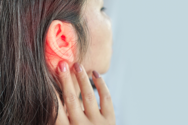A person touching their ear, which appears to be glowing red, possibly indicating ear pain or an ear infection. The person's face is not fully visible