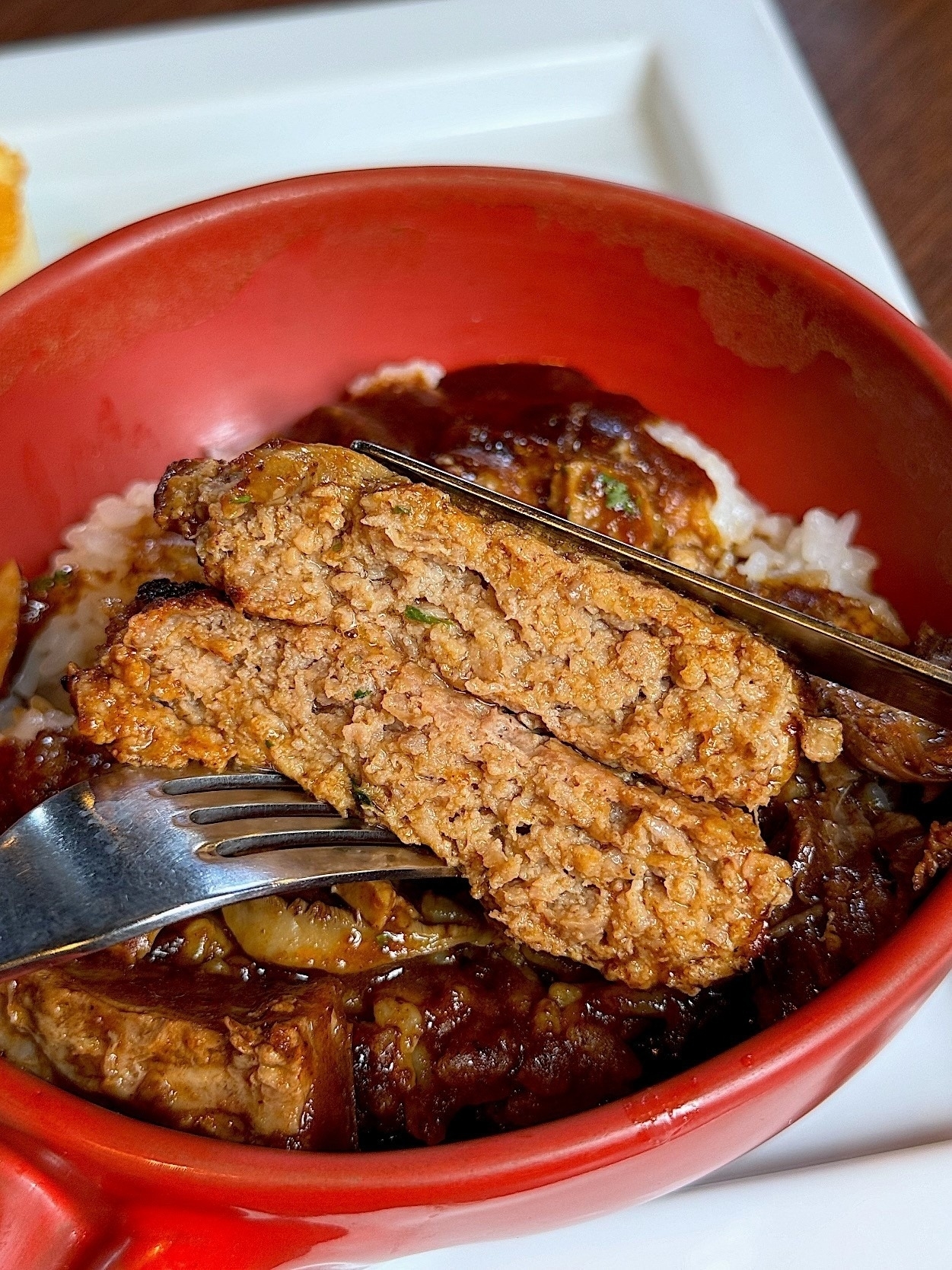 ご飯の上にハンバーグがのった料理をフォークで切っているところ。