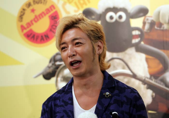 金髪の男性が、アードマンアニメーションズのイベントで話しています。背景にはアードマンツアーのロゴと羊のショーンのキャラクターが描かれています。