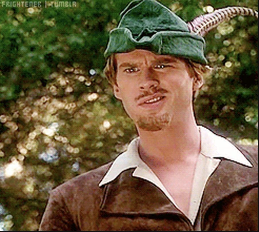 A person dressed as Robin Hood, wearing a green hat with a feather, a brown coat with a white collar, and a thin mustache and beard