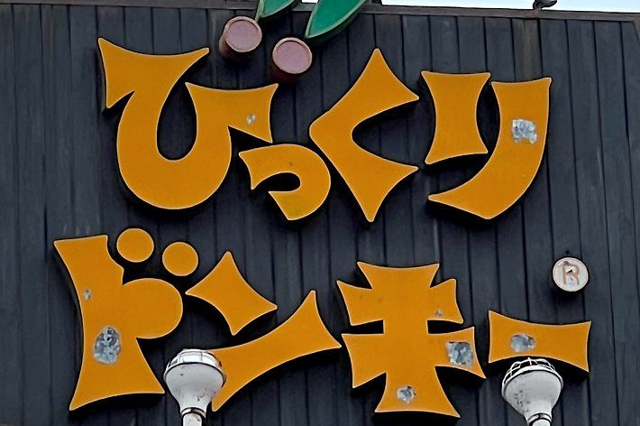 A large outdoor sign with Japanese text that reads &ldquo;びっくりドンキー&rdquo;. The sign features decorative elements including green shoes and a red ball