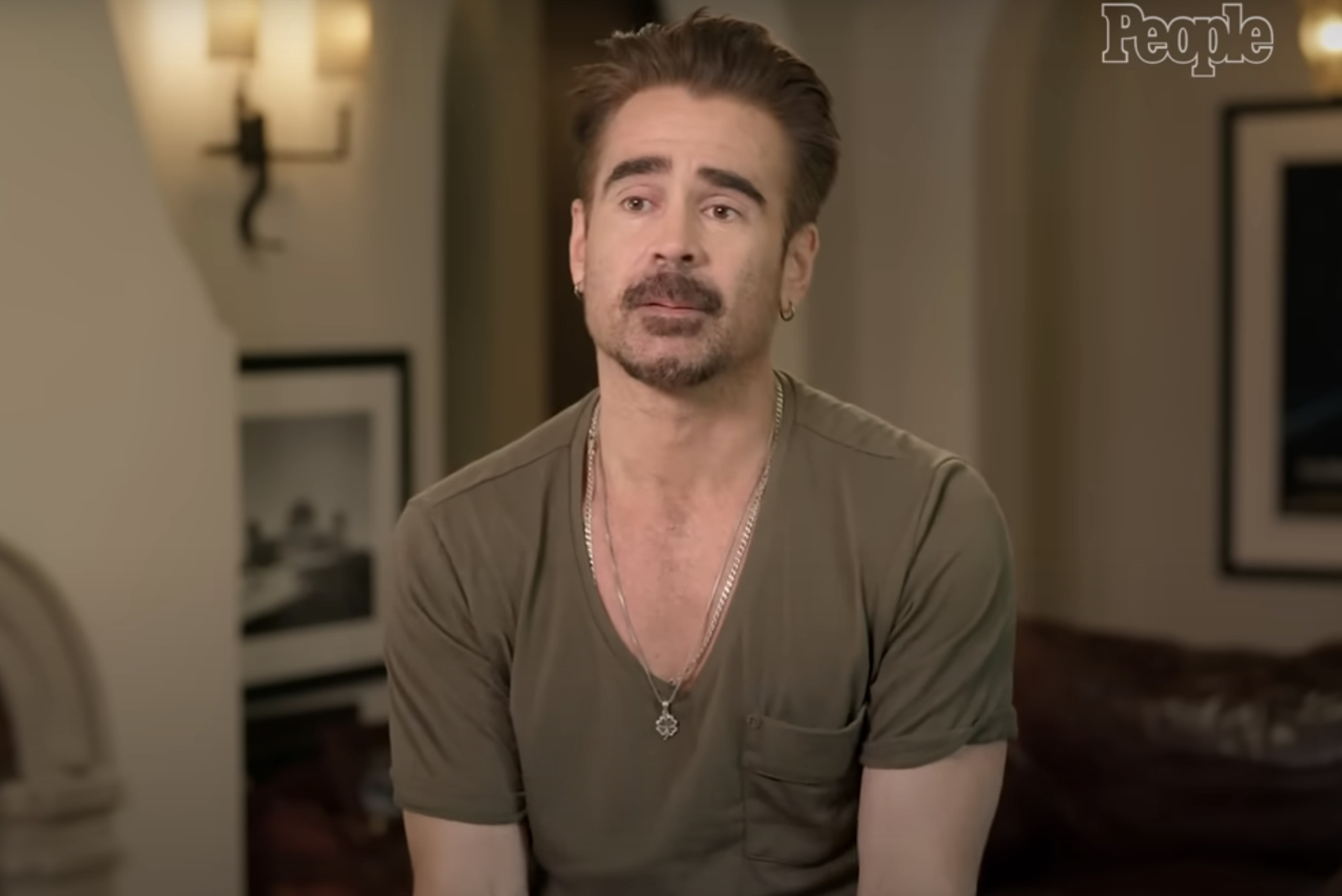 Colin Farrell, in a casual shirt with rolled-up sleeves, looks ahead while seated indoors for a People interview