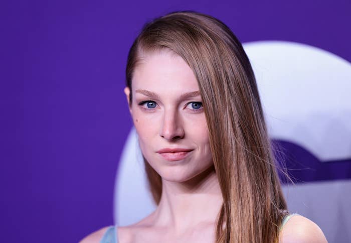 Hunter Schafer poses in front of a purple backdrop. She is wearing a simple, elegant dress
