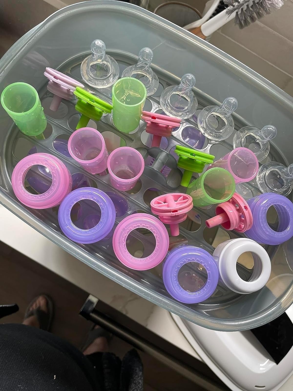 Various babe  vessel  parts and pacifiers successful  a drying rack, featuring nipples, rings, and caps successful  pastel colors