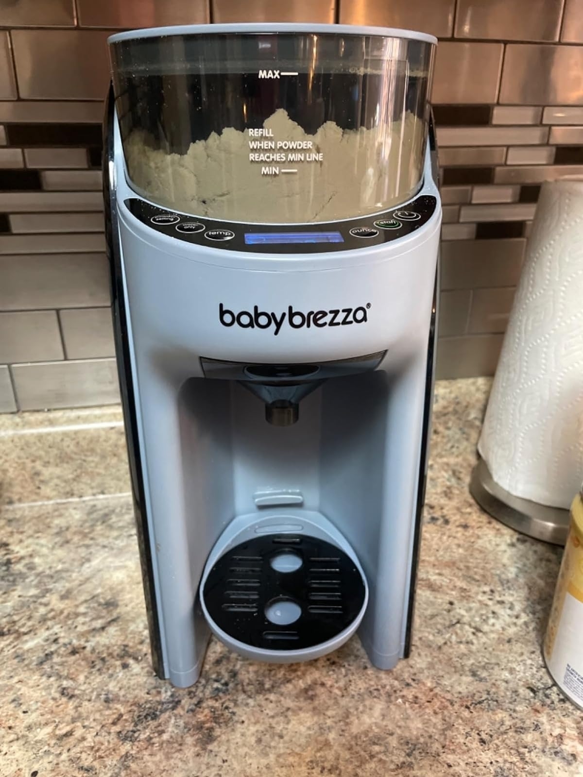 Baby Brezza Formula Pro on a kitchen countertop with a paper towel roll in the background. It automates baby formula preparation