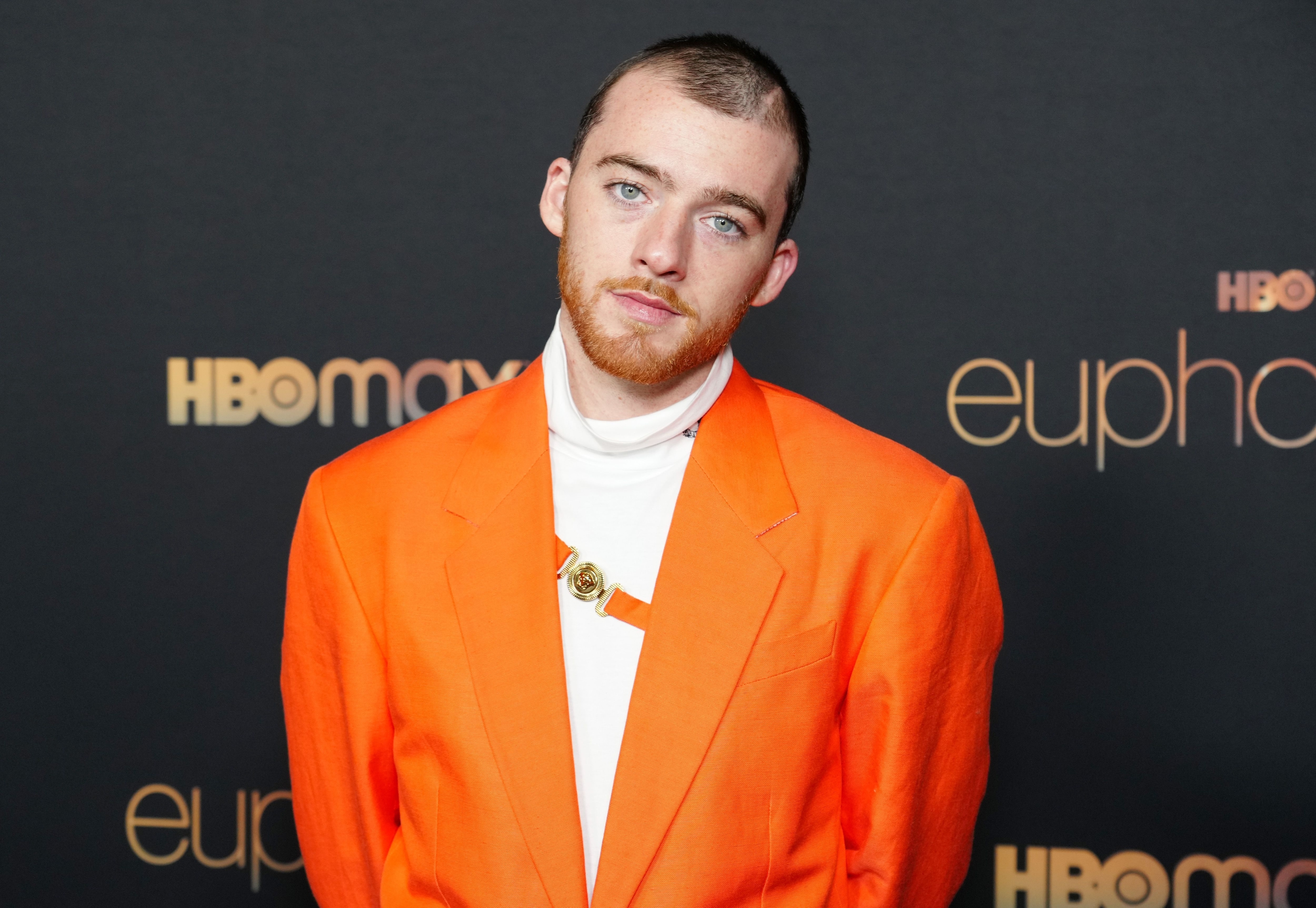 Angus Cloud poses on the red carpet in a bright orange suit at an event for HBO Max's "Euphoria"