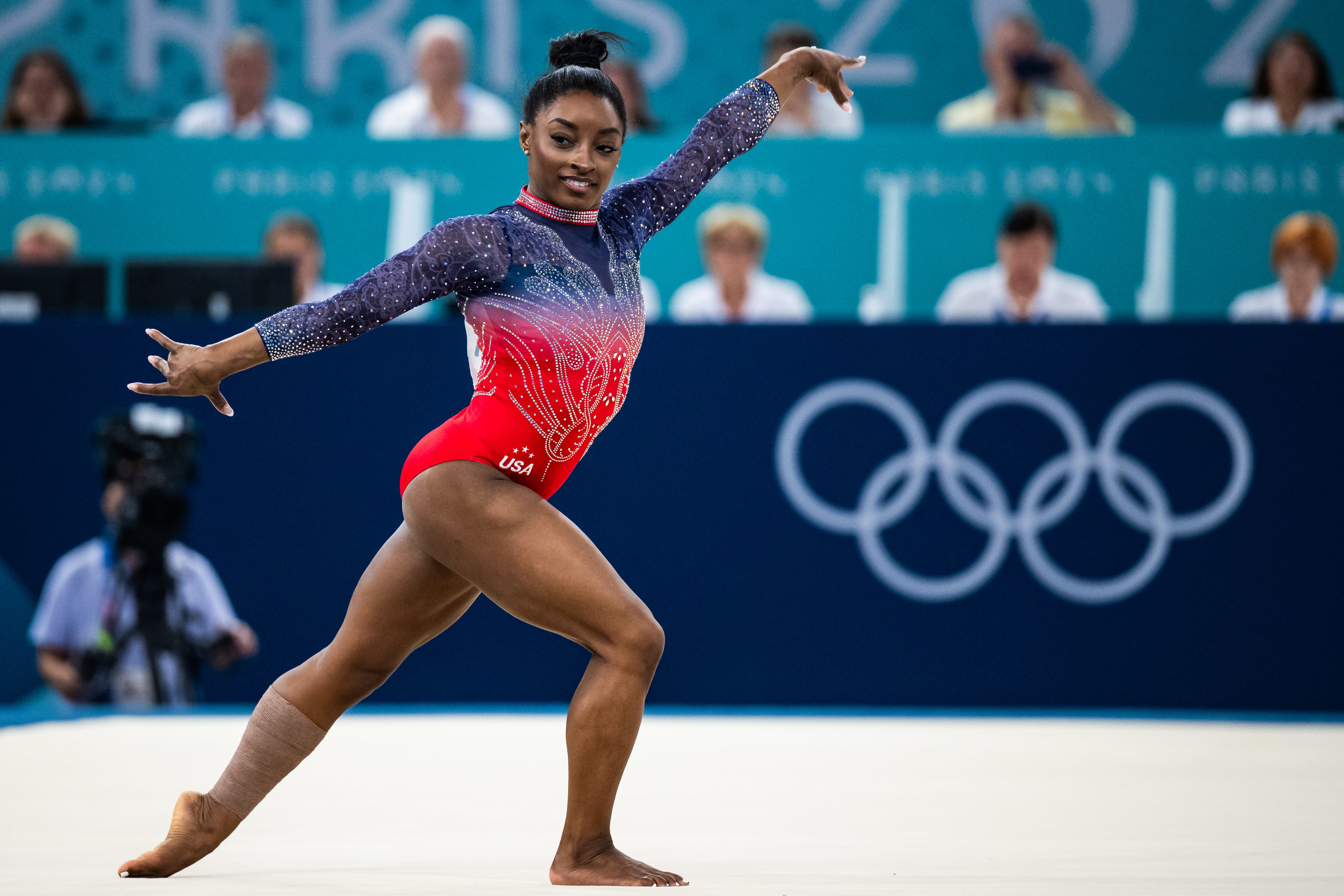 Simone Biles performs a gymnastics routine at an Olympic event, wearing a leotard with intricate designs