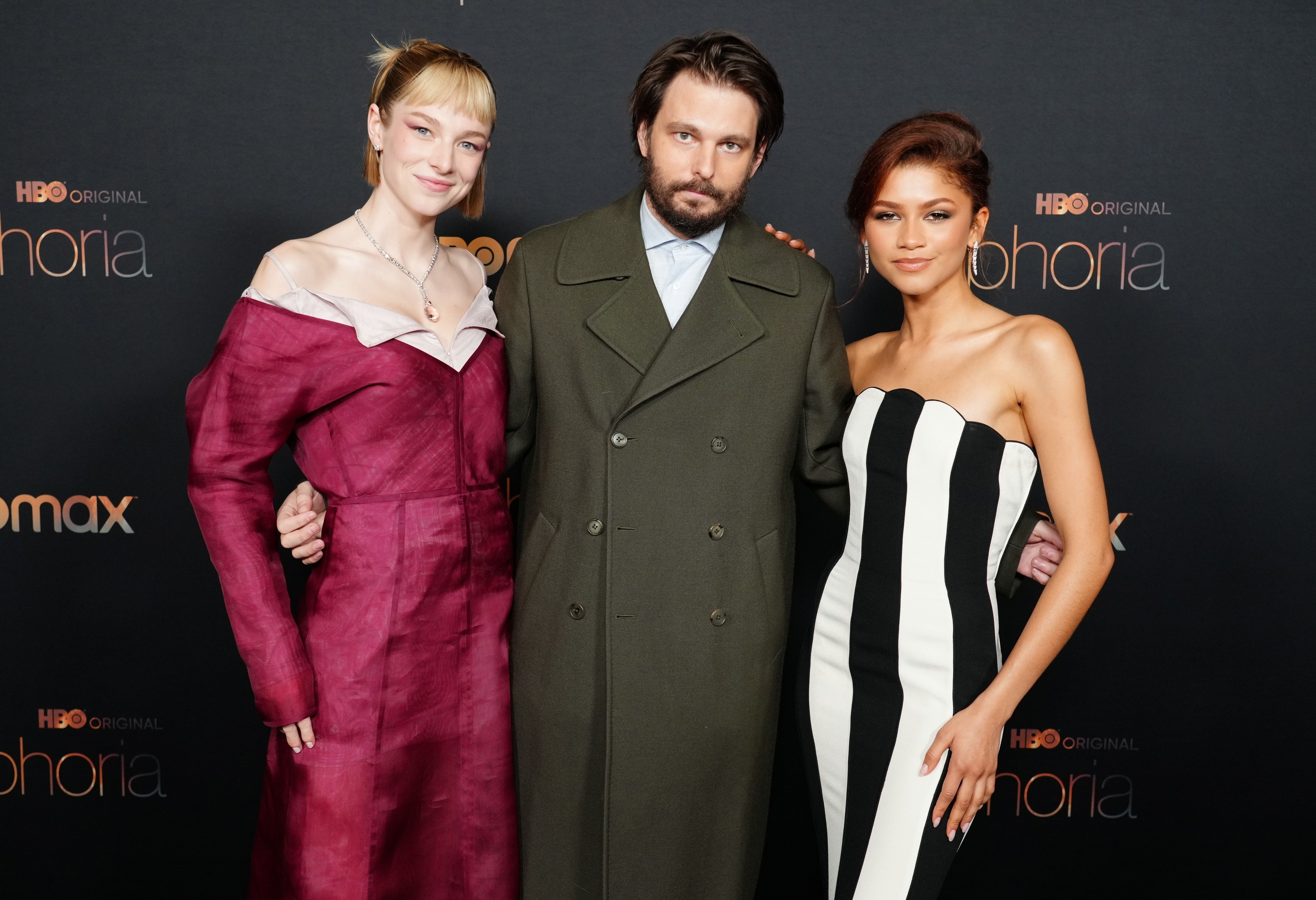 Hunter Schafer, Jacob Elordi, and Zendaya pose together on the red carpet. Hunter is in a structured gown, Jacob in a coat, and Zendaya in a strapless dress