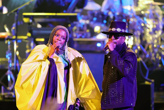 Lauryn Hill and Wyclef Jean performing on stage, Lauryn in a dramatic cape and Wyclef in a studded jacket and hat