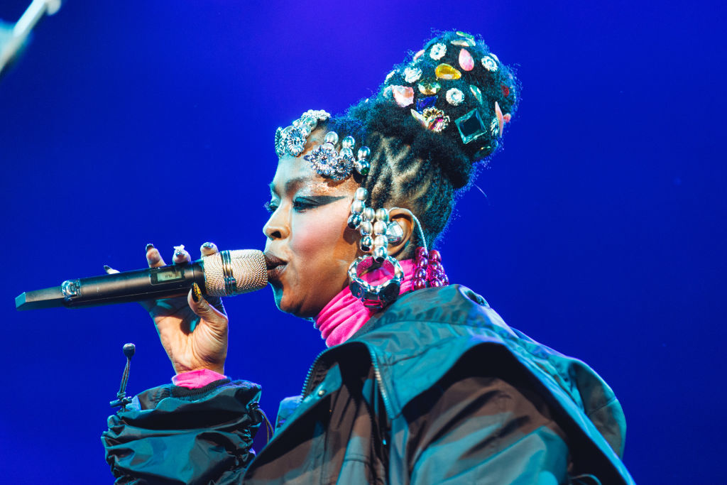 Lauryn Hill performs on stage, wearing an elaborate headpiece and stylish outfit