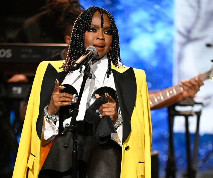 Lauryn Hill performs on stage wearing a jacket over a shirt with dark accents