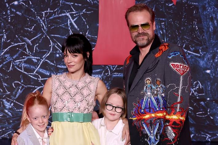 Lily Allen and David Harbour pose on a red carpet with two children. Lily wears a sleeveless dress, and David wears a decorated suit with embroidered designs