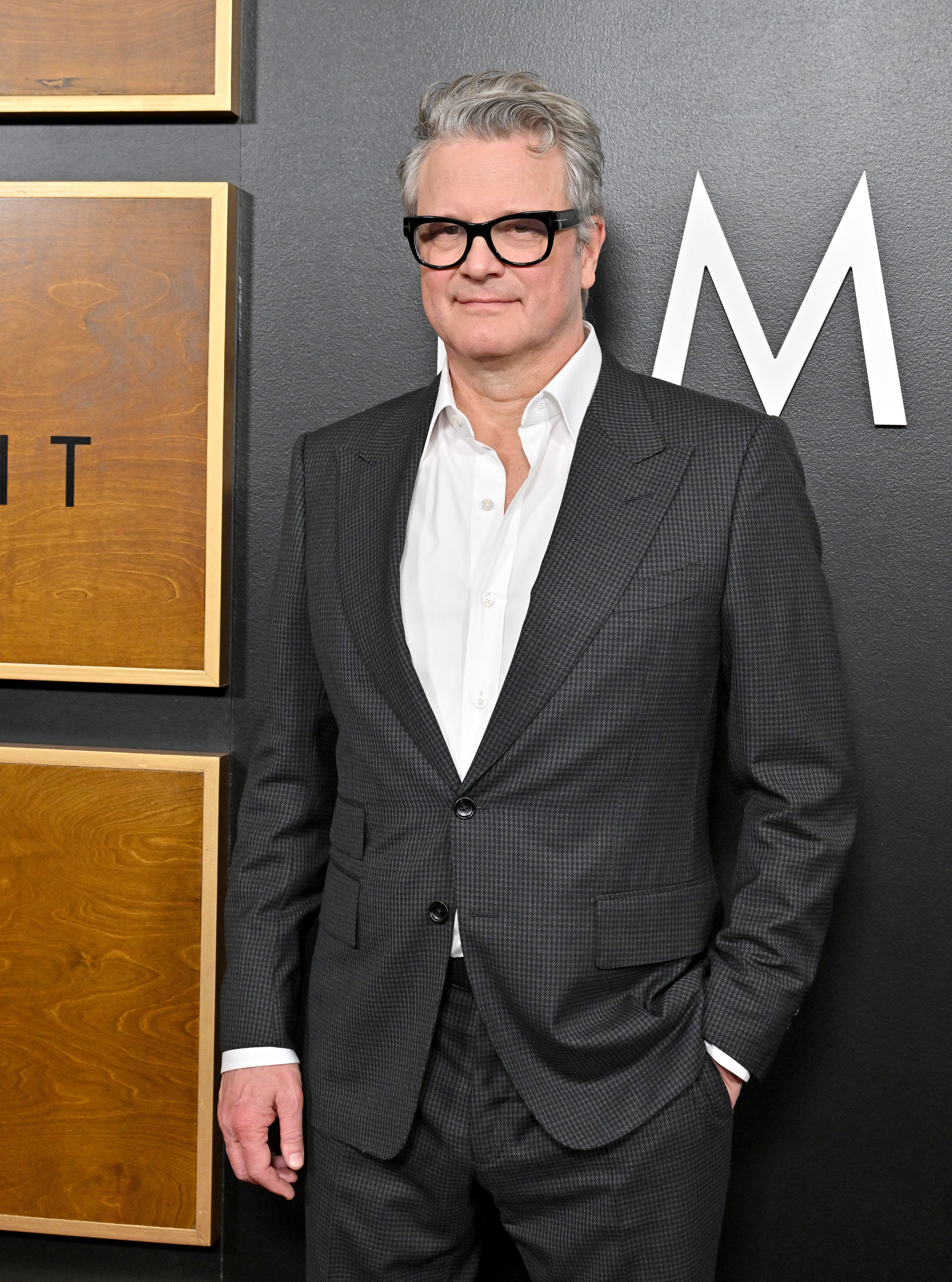 Colin Firth poses in a checkered suit and white shirt at a black carpet event