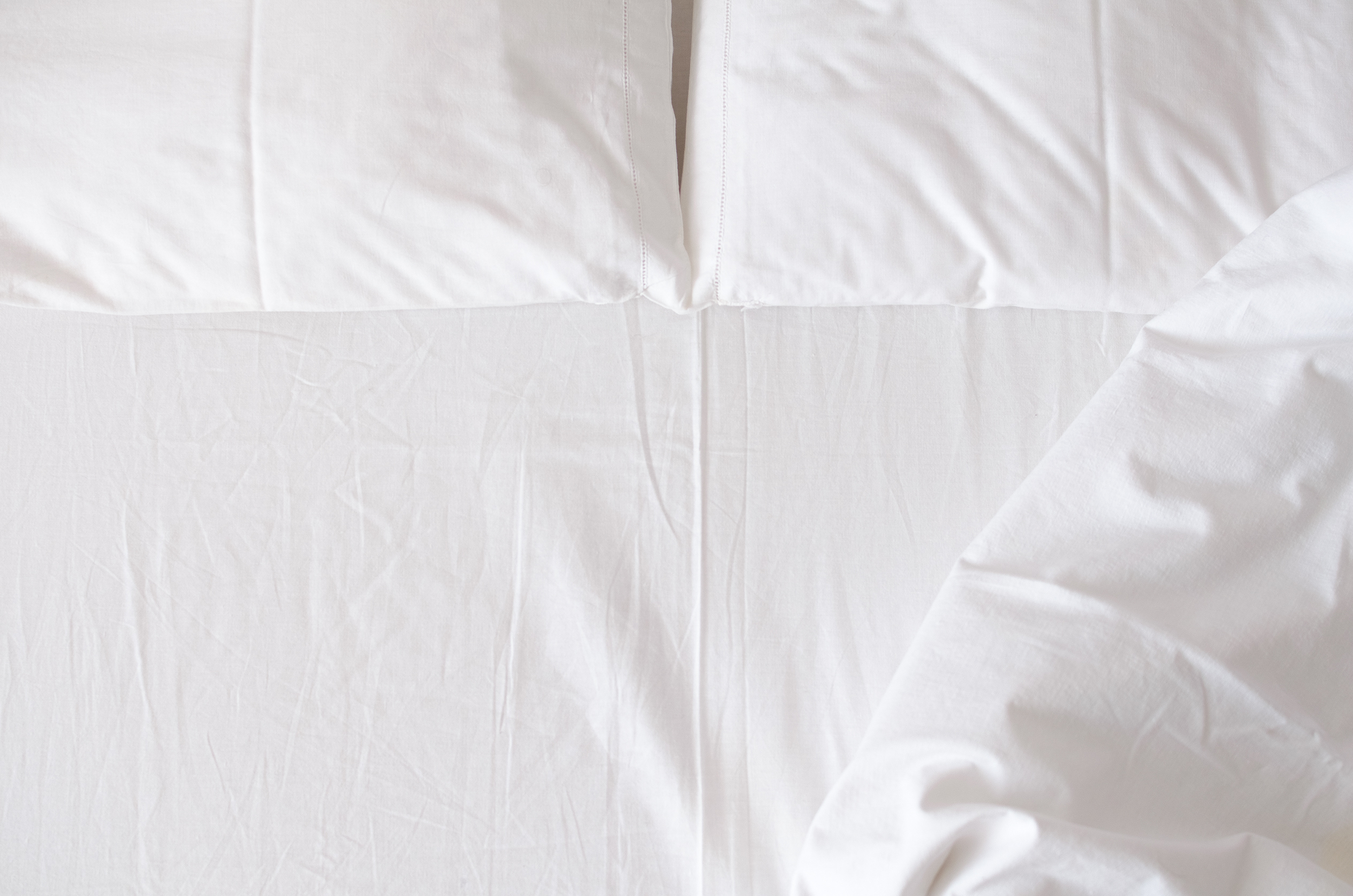 A neatly made bed with white sheets and pillows, with part of the blanket slightly turned down on the right side