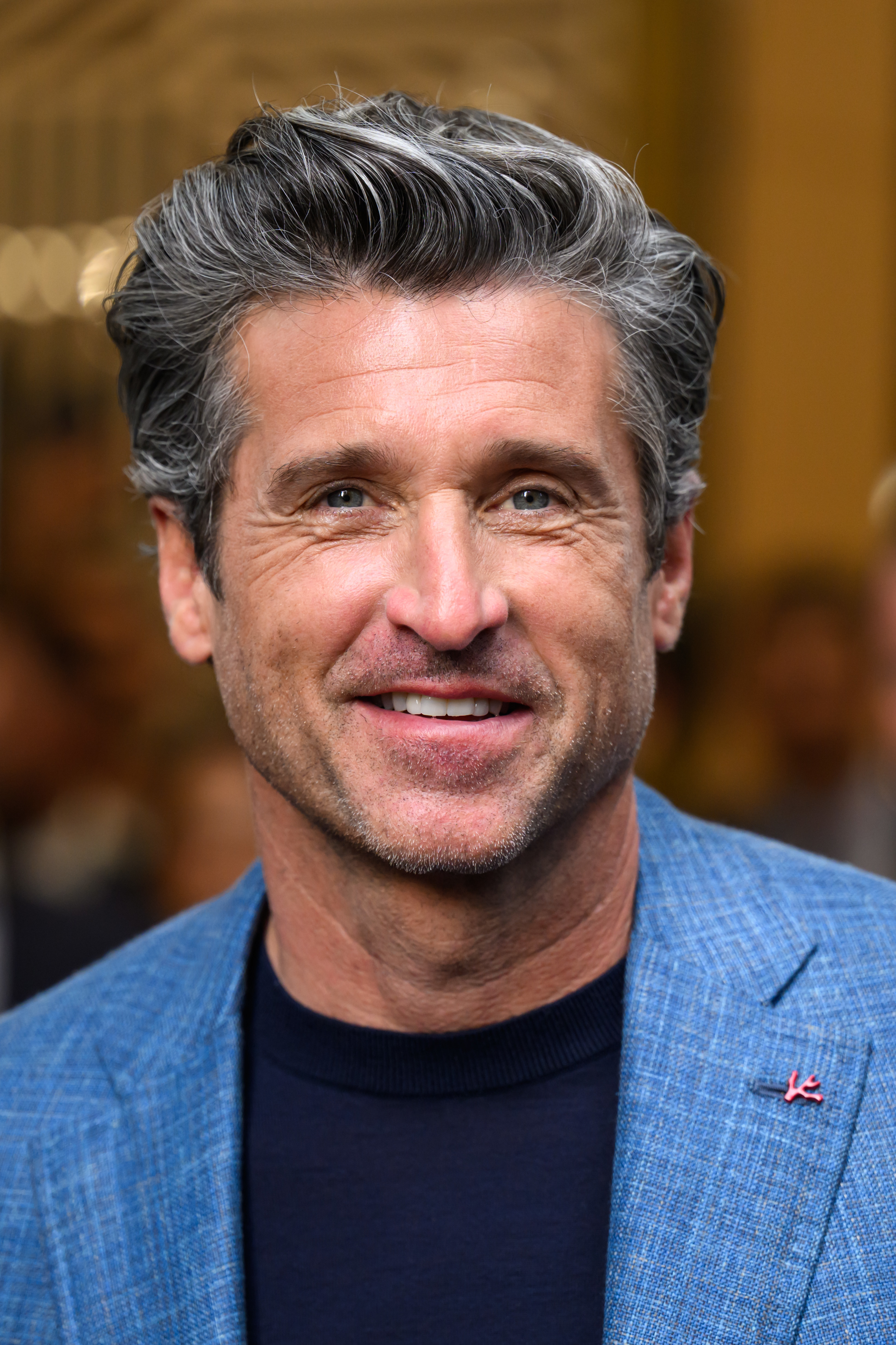 Patrick Dempsey smiling at an event, wearing a blue blazer over a dark shirt