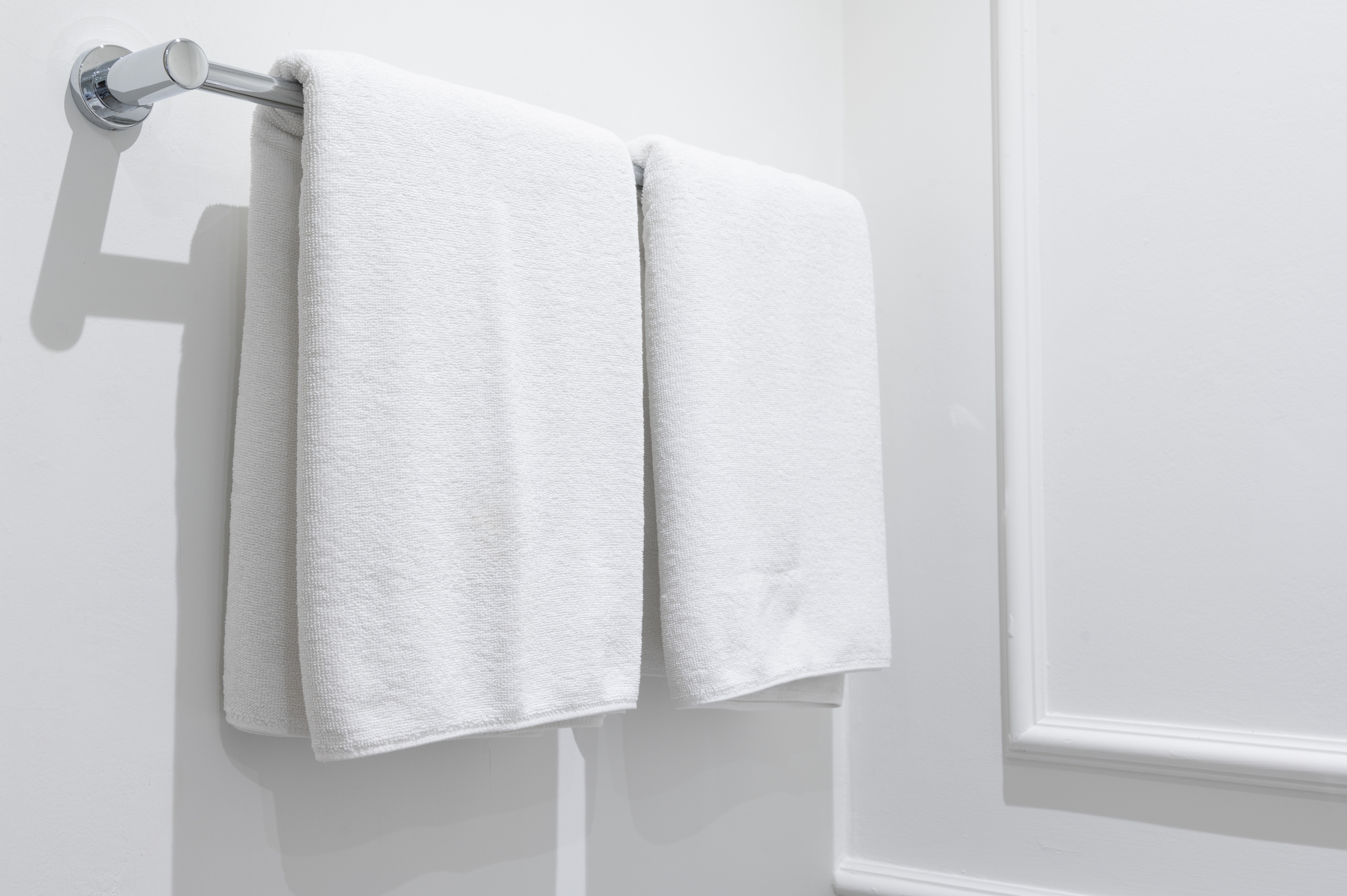 Two white towels hang neatly side by side on a silver towel rack in a minimalist bathroom setting