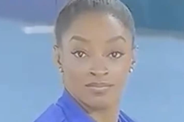 Simone Biles is seen in a close-up shot, wearing a blue outfit, with her hair neatly tied back. She is looking directly at the camera